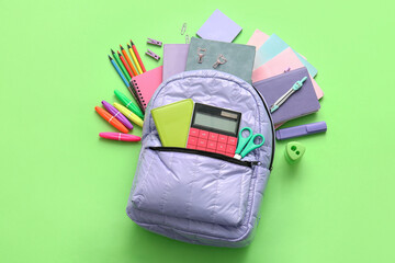 Lilac school backpack with different stationery supplies on green background