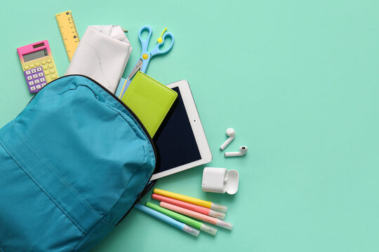 Blue school backpack with different stationery supplies, earphones and modern tablet computer on turquoise background