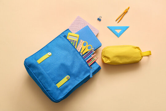 Blue school backpack with different stationery supplies on beige background