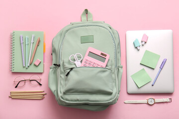 Green school backpack with different stationery supplies, wrist watch and modern laptop on pink...