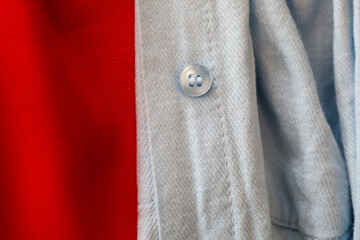 Blue shirt fabric with a single button in close-up, contrasting with a bright red background. This...