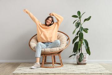 Young woman with headphones listening to music in cocoon chair near light wall