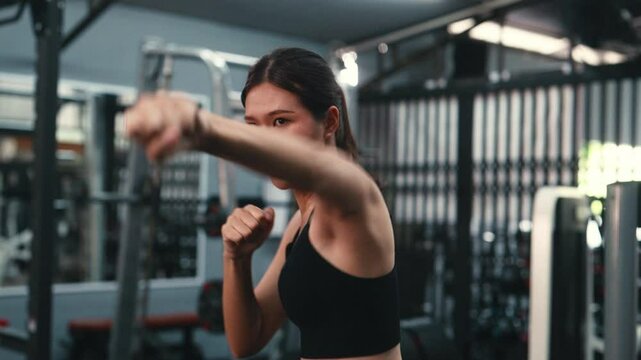 Female boxer training intensely, performing punching techniques inside modern fitness center with professional boxing equipment