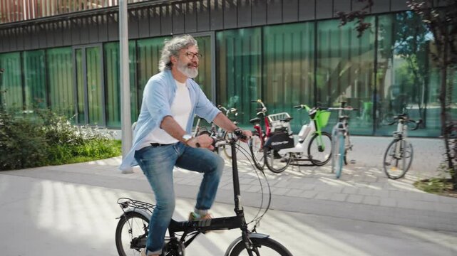 Happy active senior man cycling on city street riding foldable electric bicycle