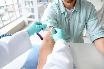 Doctor applying tourniquet on donor's arm before blood transfusion at table in clinic, closeup