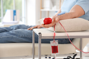 Young man with heart donating blood in clinic, closeup