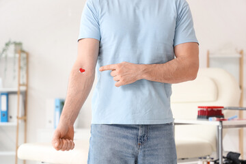 Young man pointing at applied patch after donating blood in clinic