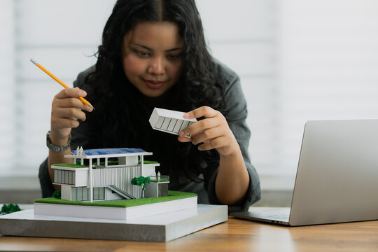 An architect is explaining a design detail, holding a component and a pencil next to a modern architectural model