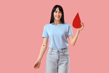 Female blood donor with medical patches and paper drop on pink background