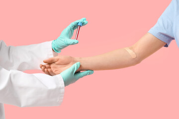 Doctor's hands with test tube and blood donor on pink background