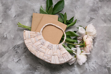 Composition with wicker bag, books and peony flowers on grey grunge background, closeup