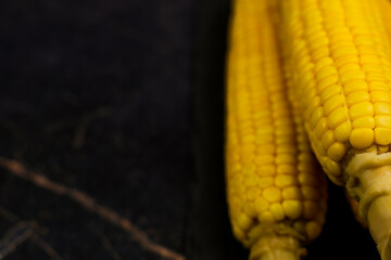 Close-up of honor yellow ripe peeled corn cobs with large grains and trunk legs on a dark background with space for text. The concept of healthy nutrition, natural iron, corn cultivation. High quality