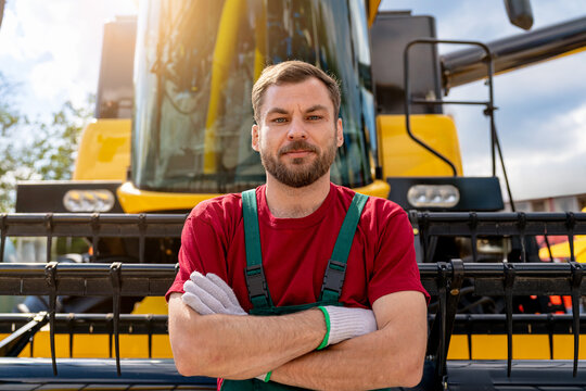 Confident male combine operator standing in front of combine harvester.