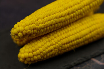 Close-up of yellow, ripe, peeled ears of corn with large grains lying sideways against a dark background in the center. The concept of healthy nutrition, natural iron, corn cultivation. High quality