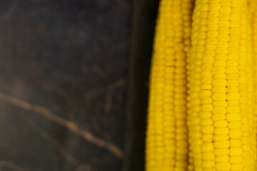 Close-up of yellow ripe peeled ears of corn with large grains lying on the side on a dark background with space for text. The concept of healthy nutrition, natural iron, corn cultivation. High quality