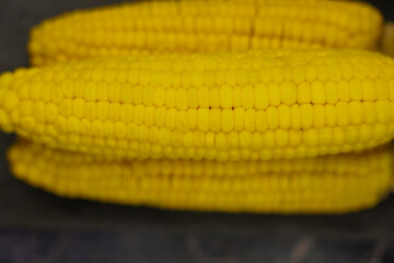 Close-up of yellow peeled ears of corn with large grains lying horizontally on a dark background in the center, focus on the top cob. The concept of healthy nutrition, natural iron, corn cultivation