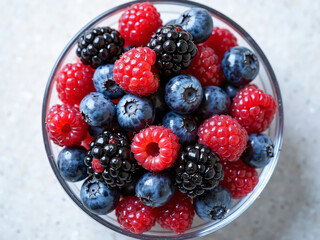 "Mixed berries (blueberries, raspberries, blackberries) in a glass bowl, top-down view"