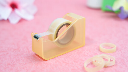 Adhesive tape dispenser with clear tape and elastic bands on a soft pink background