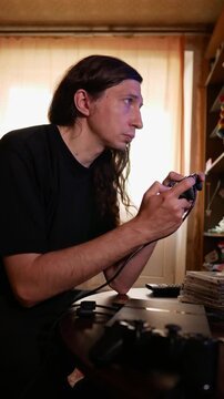 An intense and concentrated mood is captured as a man with long hair plays a video game using a controller, his profile sharply focused on the screen, reflecting deep immersion in the game