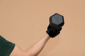 A person’s arm wearing a black gym glove while lifting a hexagonal black dumbbell against a clean beige background