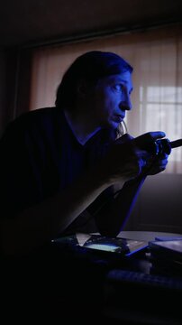 An intensely concentrated and immersive mood is captured as a man with long hair plays a video game on an older television in a dimly lit room, his face illuminated by the screen's glow