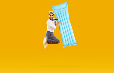 Funny excited happy man wearing office clothes with shirt and tie holding inflatable mattress and having fun jumping isolated on yellow background. Happy tourist is going on summer holiday trip.