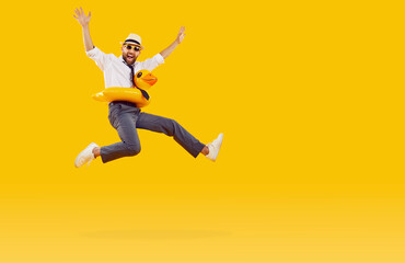 Fototapeta premium Funny cheerful businessman with inflatable swimming circle having fun on orange background. Full length of joyfully excited millennial office worker jumping high while enjoying summer vacation. Banner