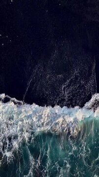 Aerial looking down at waves on a black sand beach in Bali Indonesia. Vertical Video.