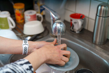 Hands washing dishes in a kitchen sink during a bright afternoon in a cozy home environment