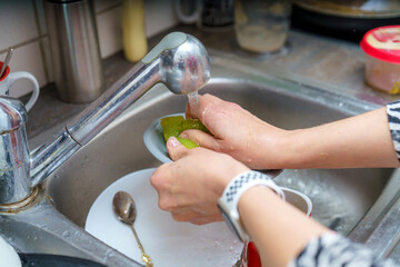 Hands washing limes in a kitchen sink while preparing ingredients for a meal during daylight hours