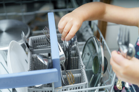 Young child organizes cutlery in a dishwasher during kitchen cleanup after a family meal