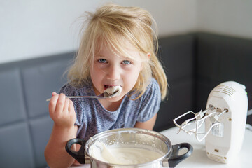Young girl enjoys sweet cream while baking in a cozy kitchen during the afternoon