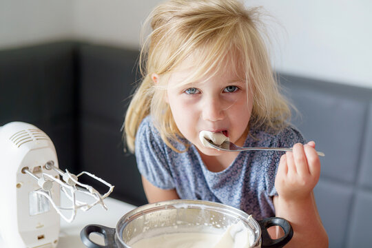 Girl tasting whipped cream in a modern kitchen during a baking activity