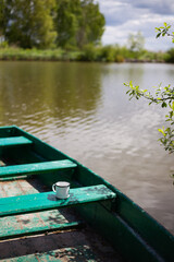 A tranquil scene of a green rowboat on still water, with a simple enamel mug resting on the wooden...