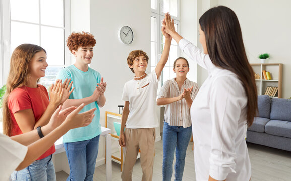 Teacher is giving a high five to a student, surrounded by happy, applauding children in a school setting. Highlights teamwork, smiling faces, and the positive atmosphere of a group. - Powered by Adobe