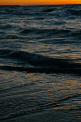 Ocean with waves, sunset sky is orange. water is choppy and waves are crashing on shore. beauty in nature, wild sandy beach at sunset. vacation or travel.