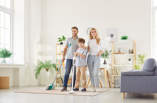 Happy friendly active family portrait enjoy doing house work together, clean carpet, wash floor in modern living room interior, tidy cleaner holding mop at home for housekeeping, household cleaning