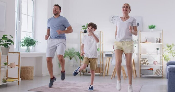 Active, sporty parents and child having a family workout at home. Happy mother, father and son boy doing a jumping exercise together in the living room. Fitness and healthy lifestyle concept