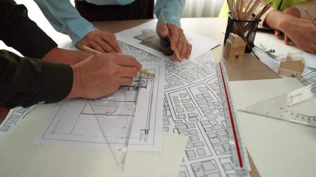 Smart architect and safety engineer discussion about building blueprint on table with architectural document, measurement tools and wooden block scatter around at modern office. Closeup. Delineation.