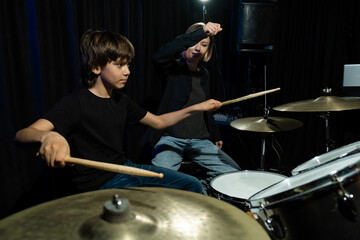 Young caucasian woman teaches a boy to play the drums in the studio on a black background. Music school student