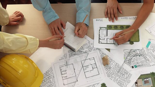 Architect and safety engineer discussion about building construction use blueprint on table with architectural document, measurement tool and wooden block scatter around at modern office. Delineation.