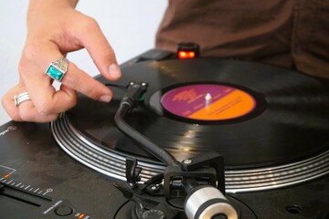 Hand von DJ mit großen bunten Ringen über Plattenteller beim Auflegen auf Party