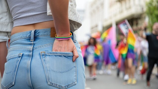 Woman wearing a rainbow bracelet on pride parade, celebrating lgbtq+ rights and community visibility, with colorful flags waving in background.