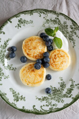 Cottage cheese pancakes or syrniki with blueberries and sour cream decorated with mint leaves, lying on beautiful vintage plate