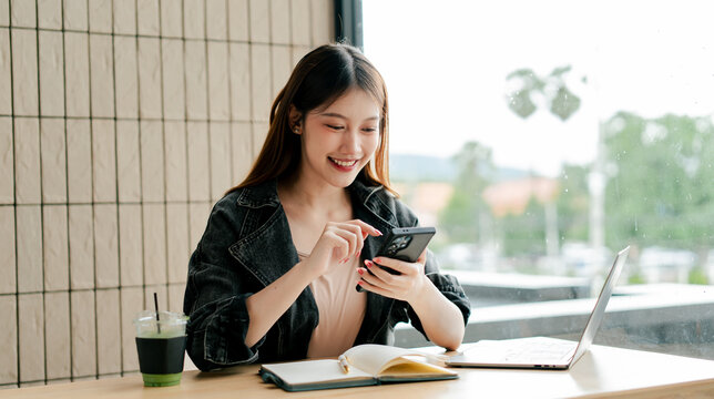 Beautiful Asian woman holding smartphone, typing text, chatting with friends, video calling on social networks. Concept of using mobile applications, online shopping, surfing, ordering food. - Powered by Adobe