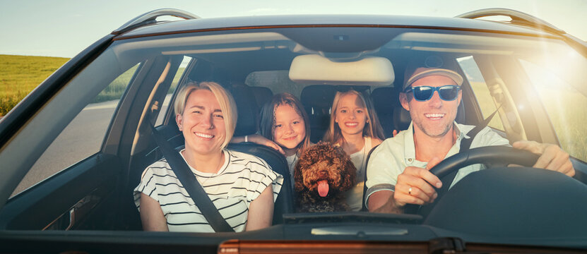 Happy family enjoys road trip together, with fluffy brown Maltipoo dog in front seat and two young girls in back. Scene captures the joy and warmth of family outing in their car - Powered by Adobe