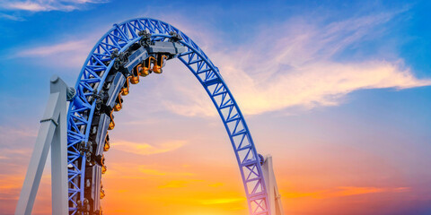 Roller coaster cart and people riding it goes through a loop upside down sky clouds vibrant color sunset.