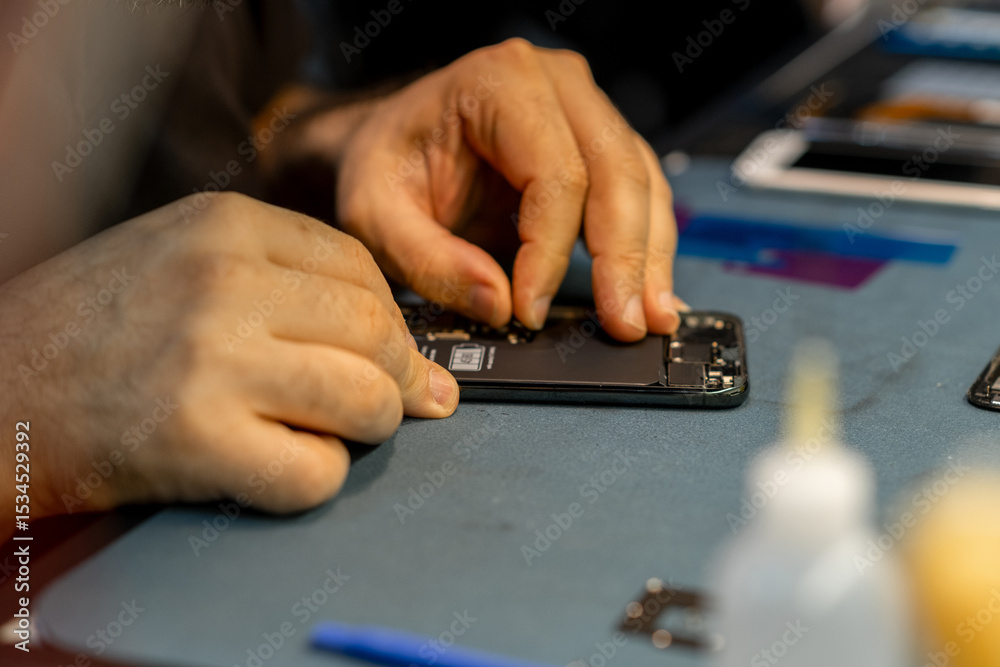 Poster expert technician repairing phone at a workspace with tools and components in a well-lit environment