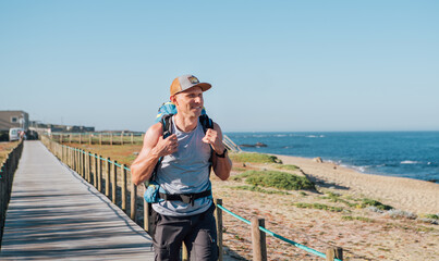 Lonely backpacker smiling man walking by sandy Portugese beach in morning. Path leading by wooden...