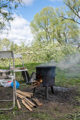 Cooking Outdoors With a Pot Over an Open Fire in a Lush Green Setting Surrounded by Trees and a Few...
